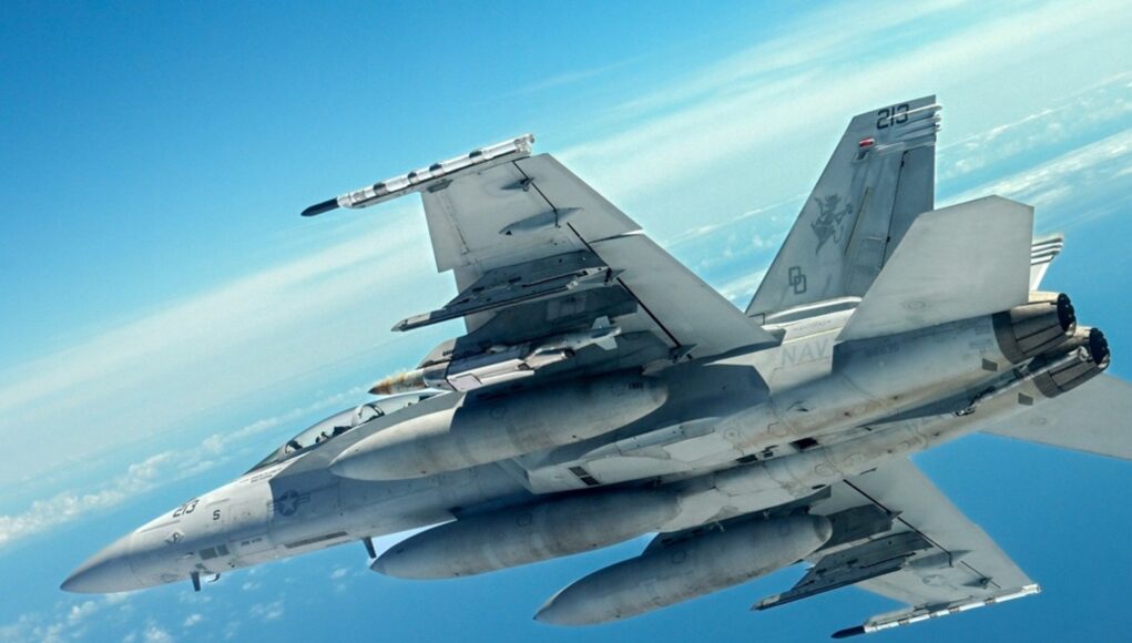 JDAMhighres Two gray military fighter jets flying in close formation across a clear blue sky, with missiles mounted under the wings and contrails in the distance.