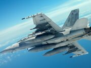 Two gray military fighter jets flying in close formation across a clear blue sky, with missiles mounted under the wings and contrails in the distance.
