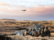 Troops and fighter jets in live fire exercise on Falklands Soldiers in camouflage crouch behind rocks on a barren landscape as a fighter jet flies overhead in the sky.