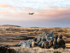 Troops and fighter jets in live fire exercise on Falklands Soldiers in camouflage crouch behind rocks on a barren landscape as a fighter jet flies overhead in the sky.