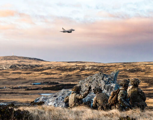 Troops and fighter jets in live fire exercise on Falklands Soldiers in camouflage crouch behind rocks on a barren landscape as a fighter jet flies overhead in the sky.