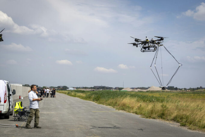 NATO tests autonomous drones without GPS Man operating a large multi-rotor drone hovering over a paved airfield beside a grassy field.