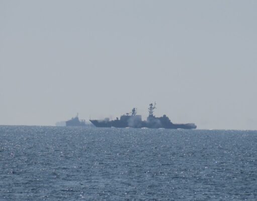 Russian warship opens fire near UK as British ship closes in Two warships sailing on the open sea near the horizon, silhouetted against a pale sky.