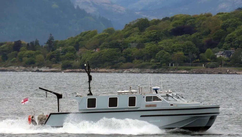 SMB Salamander seen operating in good conditions Gray cabin cruiser speeding across a bay with a tree-lined shoreline in the background, creating wake in the water.