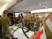 Military medics gathered around a patient on a stretcher inside a military aircraft, preparing a medical evacuation.