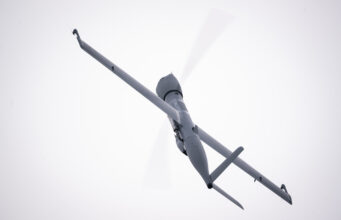 Airbus Flexrotor begins Baltic maritime surveillance work View of a gray helicopter seen from below with spinning rotor blades against a pale sky.