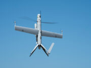 Unmanned aerial vehicle (drone) with a fixed wing and helicopter-style rotor against a blue sky in flight.