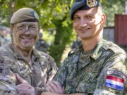 Yorkshire officer cadets train with Dutch in Netherlands Two soldiers in camouflage shake hands and smile, with more troops visible in the background outdoors.
