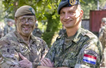 Yorkshire officer cadets train with Dutch in Netherlands Two soldiers in camouflage shake hands and smile, with more troops visible in the background outdoors.