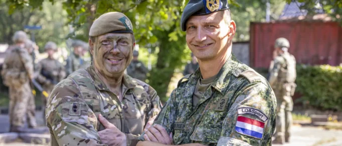 Yorkshire officer cadets train with Dutch in Netherlands Two soldiers in camouflage shake hands and smile, with more troops visible in the background outdoors.