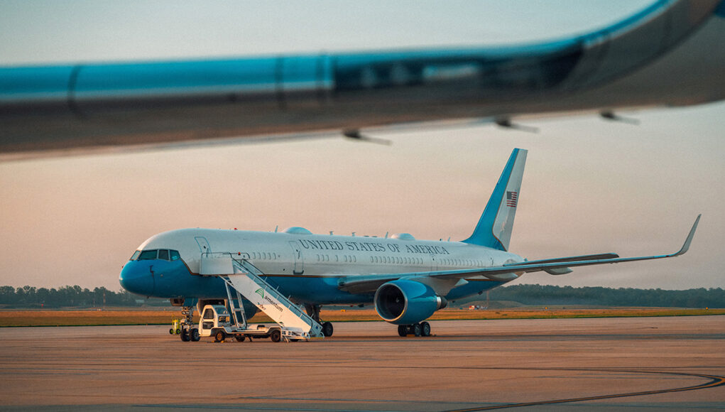 c32a United States government aircraft parked on the tarmac with mobile stairs and a blue nose, during sunset.