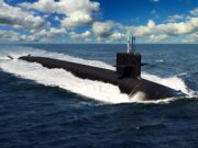 A dark submarine gliding at the ocean surface, creating a white wake with a blue sky and clouds above, a small American flag on the conning tower.