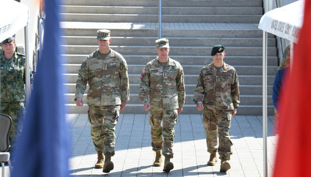 cq5dam.web.1280.1280 (16) Three soldiers in camouflage walk down a wide set of stairs, flags blurred in the foreground.
