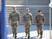 European officer to lead Ukraine aid command within a year Three soldiers in camouflage walk down a wide set of stairs, flags blurred in the foreground.