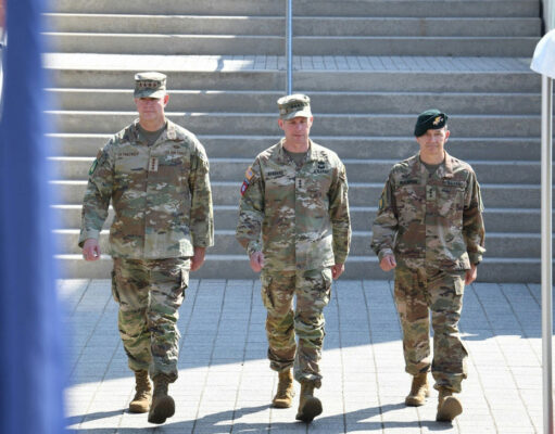 European officer to lead Ukraine aid command within a year Three soldiers in camouflage walk down a wide set of stairs, flags blurred in the foreground.