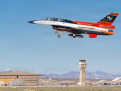 USAF Test Pilot School jet trainer with two crew taking off from an airbase; control tower in the background.