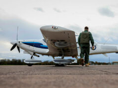 Air cadet gliders to serve to mid-century after upgrade Pilot in a green flight suit walks toward a small white-and-blue propeller plane on a runway.