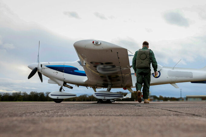 Air cadet gliders to serve to mid-century after upgrade Pilot in a green flight suit walks toward a small white-and-blue propeller plane on a runway.