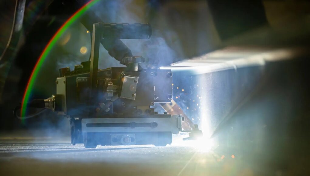hiiWELD Welding or laser-cutting machine in operation, bright light and sparks shining on a metal workpiece in a dim workshop.
