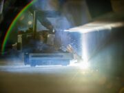 Robots to weld American warships in shipyard pilot Welding or laser-cutting machine in operation, bright light and sparks shining on a metal workpiece in a dim workshop.