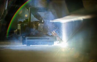 Robots to weld American warships in shipyard pilot Welding or laser-cutting machine in operation, bright light and sparks shining on a metal workpiece in a dim workshop.