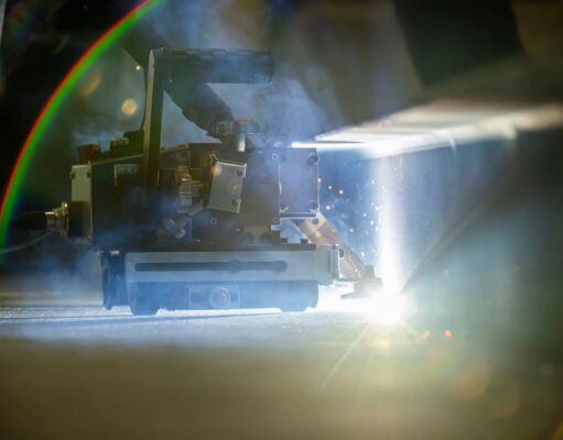 Robots to weld American warships in shipyard pilot Welding or laser-cutting machine in operation, bright light and sparks shining on a metal workpiece in a dim workshop.