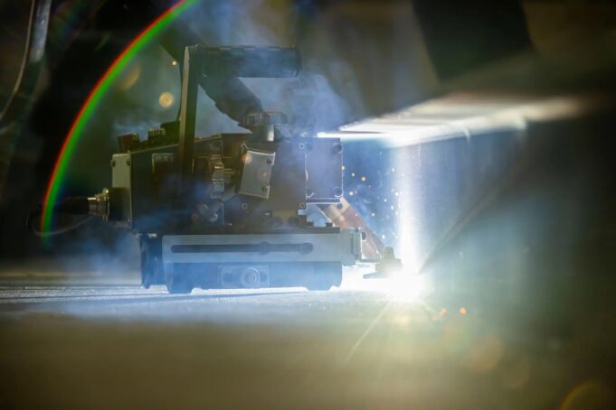 Robots to weld American warships in shipyard pilot Welding or laser-cutting machine in operation, bright light and sparks shining on a metal workpiece in a dim workshop.