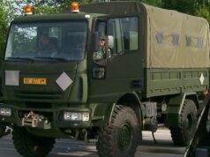 Leonardo weighs options for Iveco truck business after buyout Front three-quarter view of an olive-drab military cargo truck with a canvas-covered rear compartment driving on a road with amber warning lights overhead.