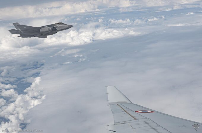 Military jet flying above clouds, seen from a passenger plane window; French Air Force markings visible on the fuselage.