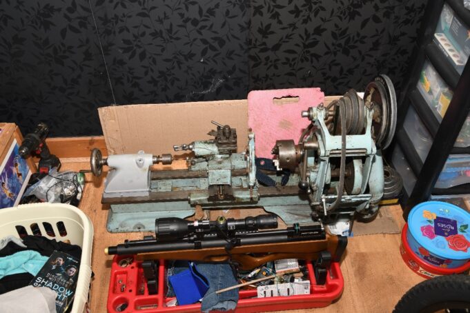 Man jailed after 3D printing gun in Shropshire A small metal lathe on a workbench with a belt-driven headstock, tooling, and a pink foam block behind it; cluttered workshop scene around it.
