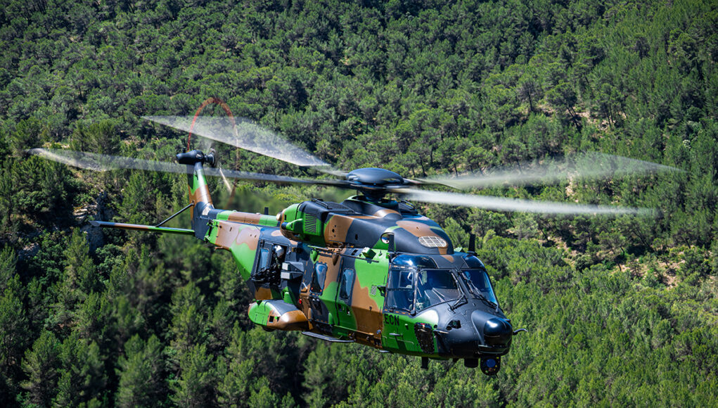 nh90-standard-2 Camouflage military helicopter in flight above a dense green forest.