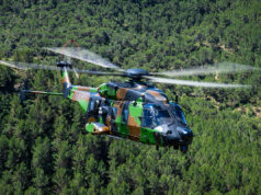 France receives first NH90 built for special operations Camouflage military helicopter in flight above a dense green forest.