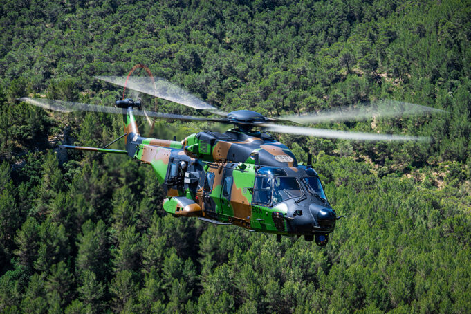 France receives first NH90 built for special operations Camouflage military helicopter in flight above a dense green forest.