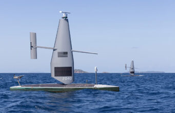 Autonomous sailing drone on a flat catamaran, a tall gray sail with the number 2040, sailing on open blue sea.
