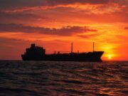 Silhouetted cargo ship on a choppy sea at sunset with an orange sky behind it