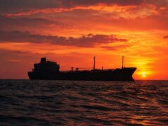 Silhouetted cargo ship on a choppy sea at sunset with an orange sky behind it