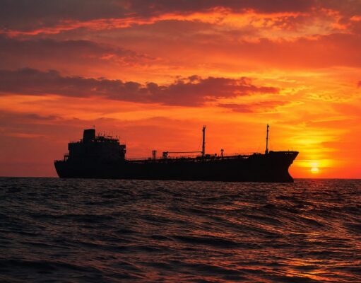 Silhouetted cargo ship on a choppy sea at sunset with an orange sky behind it