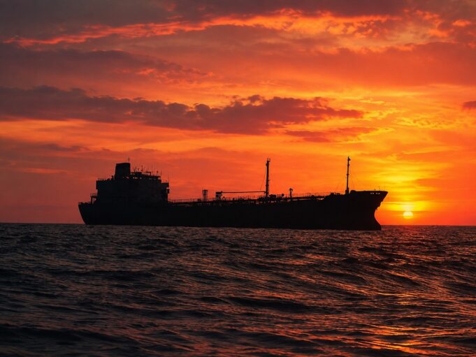 Silhouetted cargo ship on a choppy sea at sunset with an orange sky behind it