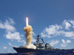 US moves to ramp up naval anti-ballistic missile production Military ship launches a rocket, bright flame and smoke plume rise from the deck into a blue sky over the ocean.