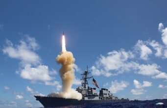 US moves to ramp up naval anti-ballistic missile production Military ship launches a rocket, bright flame and smoke plume rise from the deck into a blue sky over the ocean.