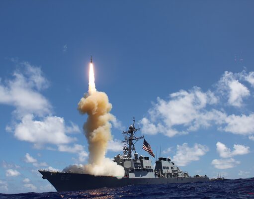US moves to ramp up naval anti-ballistic missile production Military ship launches a rocket, bright flame and smoke plume rise from the deck into a blue sky over the ocean.