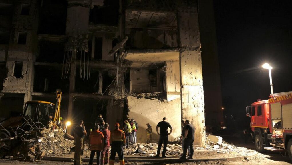 ukraine1223 Nighttime scene of a collapsed building with rescue workers and a fire truck inspecting the rubble.